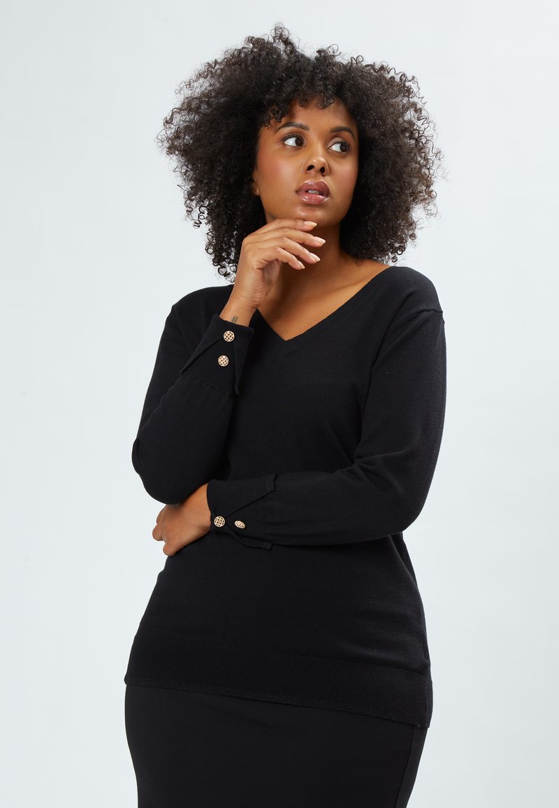 Schwarzer V-Ausschnitt-Pullover aus weichem Material, mit langen Ärmeln, die über dekorative goldene Knöpfe an den Bündchen und einem gerippten Saum verfügen.