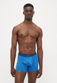 Kék boxeralsó sötétkék "Levi's" logóval díszítve, ismétlődő mintázatú, kontrasztos derékpánttal és sima, rugalmas textúrával.