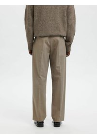 Bēša krāsas platās bikses ar teksturētu virsmu, priekšpusē ar krokām un pielāgotu piegriezumu, kombinētas ar melniem apaviem.