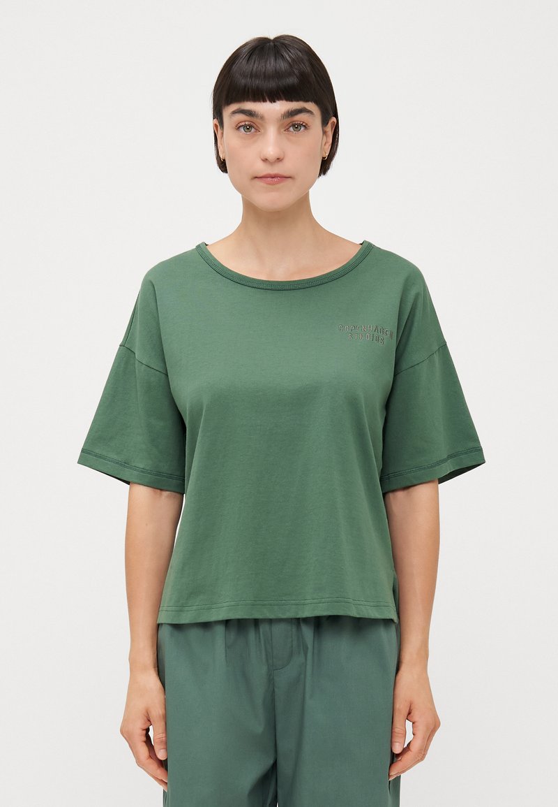 Olijfgroene katoenen t-shirt met een losse pasvorm, wijde mouwen en een ronde halslijn. Bevat een subtiel logo in donkerder groen op de borst.