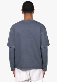 Szara, oversize t-shirt z teksturowanym wykończeniem. Posiada krótkie rękawy, okrągły dekolt oraz obniżone ramiona, co zapewnia luźny krój.