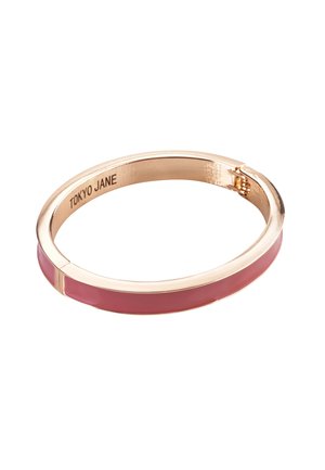 Goldfarbene Armspange mit einem glatten pinken Emailleband, das ein elegantes Design aufweist und eine kleine Öffnung zum Öffnen und Schließen hat. Mit der Gravur "TOKYO JANE."