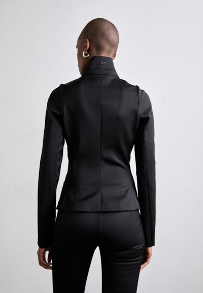 Black tailored jacket with a high collar, fitted shape, and long sleeves. Features a subtle logo detail at the collar. Smooth texture.