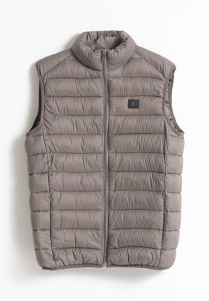 Chaleco aislante gris con cuello alto, diseño acolchado, cremallera frontal y pequeño parche de logo negro en el lado izquierdo. Textura suave.