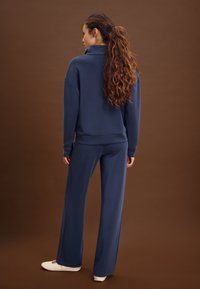 Marineblaue, locker sitzende Sweatshirt mit hohem Kragen und passende Hose. Glatte Textur, minimalistisches Design, kombiniert mit weißen Slip-On-Schuhen.