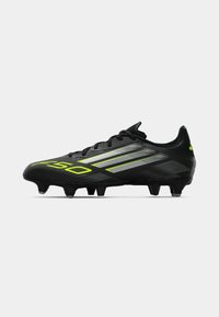 Schwarzer Fußballschuh aus strukturiertem Synthetikmaterial, mit leuchtend grünen und silbernen Streifen, markantem Design und konischen Stollen für besserenGrip.