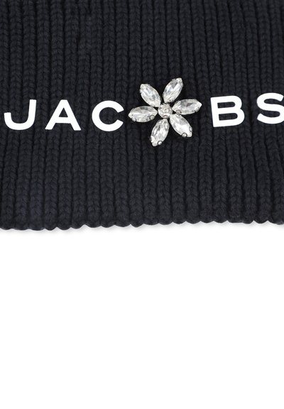 Čierna ryhovaná tkanina s bielym textom "JAC" a "BS." Obsahuje striebornú brošňu vo forme kvetu s priehľadnými, marquise rezanými kameňmi.