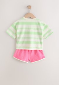 Striped cotton t-shirt in light green and white, paired with pink terry shorts. Both hang on a wooden hanger against a light background.