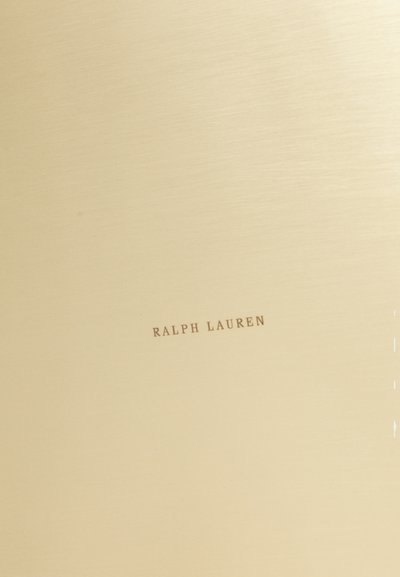 Guldtonat metalsurface med en borstad yta; har den präglade texten "RALPH LAUREN" i en brun stil nära botten.