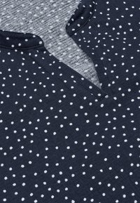 Mørkeblå stof med spredte hvide polkaprikker og en V-udskæring med notch-detalje.