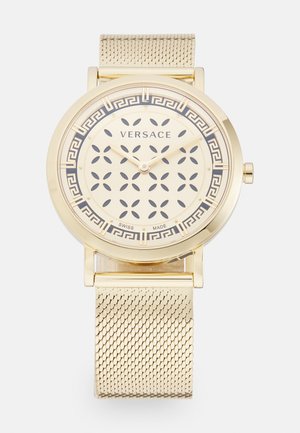 Gold Versace wristwatch with patterned dial, Greek key border, two hands, mesh metal strap, and Swiss Made label.