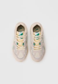 Beige sneakers with mesh upper, green accents, and reflective detailing. Flat laces and padded collar for comfort. Light-colored sole.