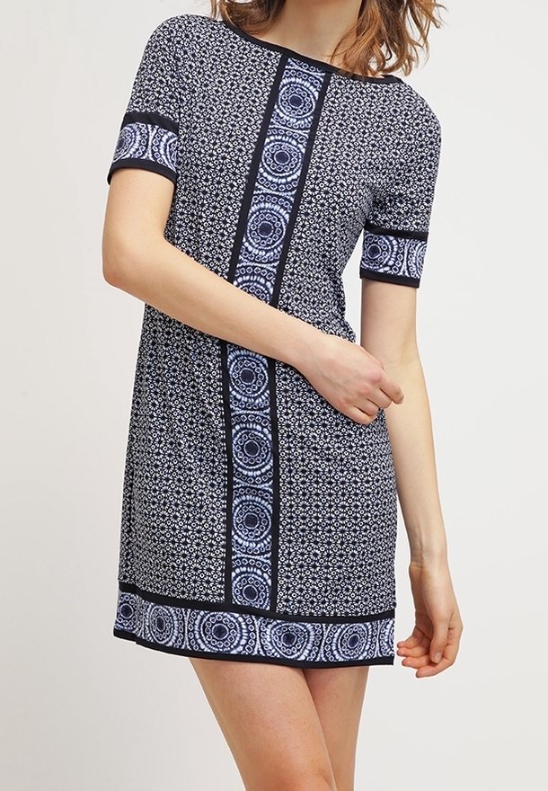 Kortärmad, marinblå klänning med blommönster och geometriska mönster, med svart kant längs sidorna och nederkanten. Slätt tyg, avslappnad passform.