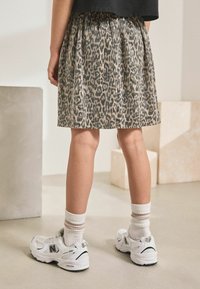 Gonna plissettata con stampa leopardata in una palette di colori beige e nero, abbinata a sneakers bianche e calzini a righe fino alla caviglia.