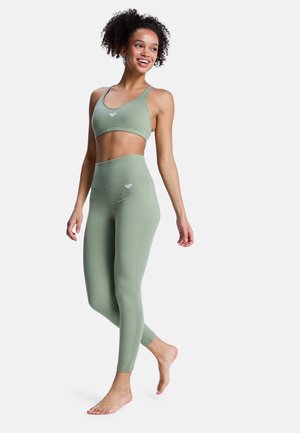 Jasnozielony sportowy biustonosz i legginsy z podwyższonym stanem wykonane z elastycznego materiału, z małym logo na przodzie obu części garderoby.