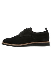 Scarpe da uomo eleganti in suede nero con rifiniture marroni sulla suola e linguetta sul tallone, mostrate in profilo laterale su sfondo bianco.