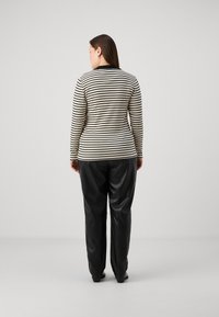 Camiseta de manga larga a rayas en crema y negro con cuello redondo, combinada con pantalones de cuero negros de corte holgado. Textura suave y diseño ajustado.