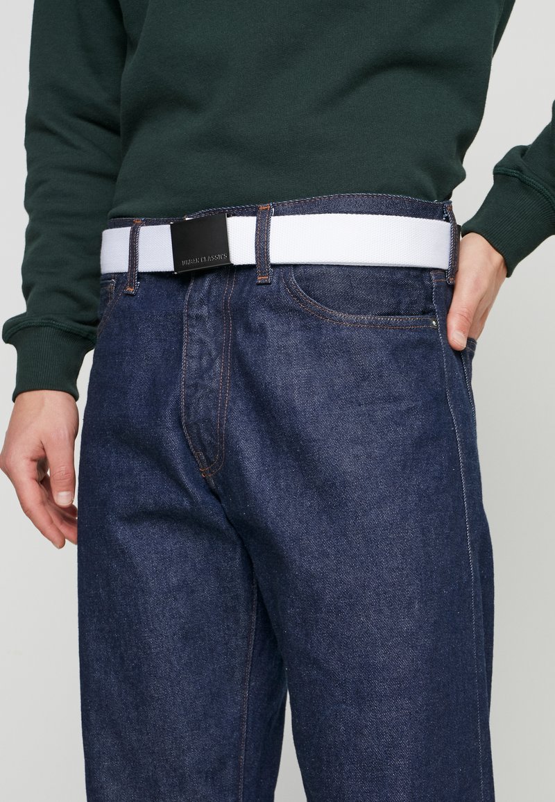 Dunkelblaue Denim-Jeans mit lockerer Passform, mit orangen Nähten und einem weißen elastischen Gürtel mit einer schwarzen Metallschnalle.