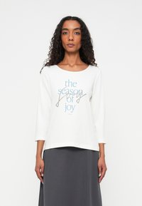 White long-sleeve shirt featuring "the season of joy" text in blue and gray, with a relaxed fit and soft cotton material.