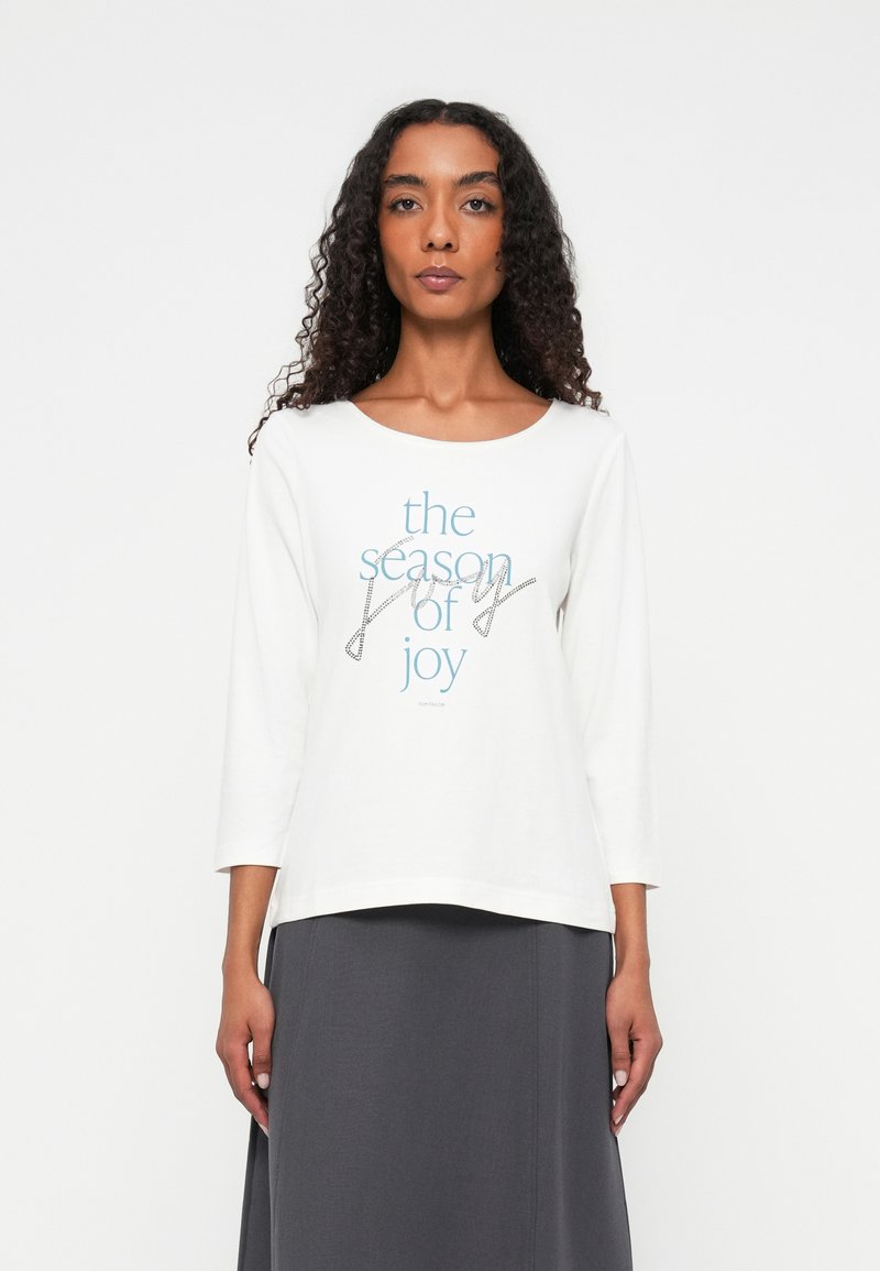White long-sleeve shirt featuring "the season of joy" text in blue and gray, with a relaxed fit and soft cotton material.