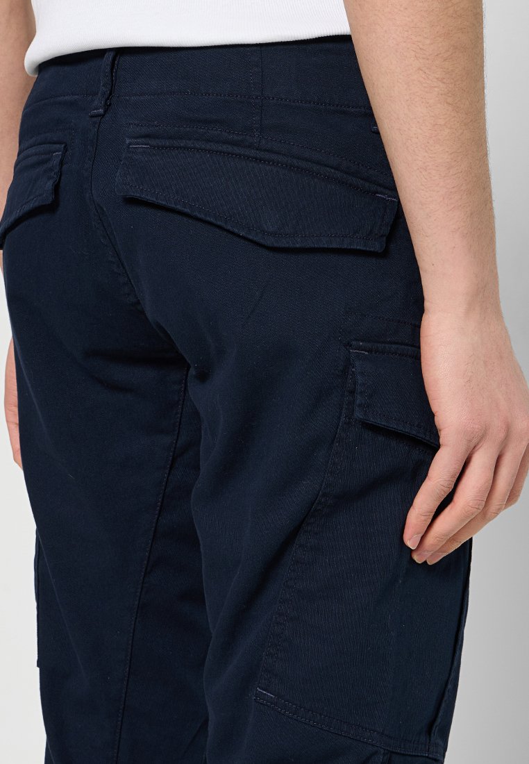 Marineblaue Cargo-Hosen aus einem glatten Baumwollgemisch, mit mehreren Taschen und verstärkten Nähten. Nahaufnahme der Details der Gesäßtasche.