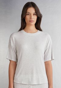 Světle šedé tričko s krátkým rukávem, volného střihu a ribovanou strukturou. Kulatý výstřih a mírně spadlé švy na ramenou.