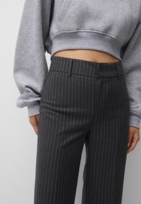Sudadera corta gris combinada con pantalones oscuros de rayas finas. Los pantalones presentan un corte ajustado y una textura suave.