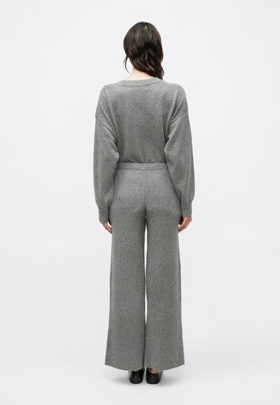 Sivý pletený sveter a súprava nohavíc s širokými nohavicami. Sveter má balónové rukávy a rebrovanú štruktúru. Nohavice sú vysokého pásu s hladkým povrchom.