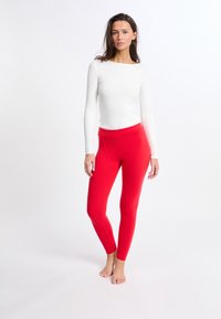 Leggings rojos hechos de tela elástica, con una textura suave y una cintura alta. Combinados con una blusa blanca de manga larga.