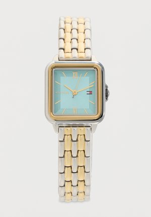 Orologio da polso con quadrante quadrato e cinturino a maglie oro e argento, quadrante azzurro chiaro, numeri romani dorati, lancette e logo Tommy Hilfiger sul quadrante.