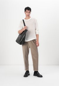 Lekki, przewiewny biały sweter z dzianiny, beżowe spodnie o tapered cut i czarna skórzana torebka na ramię. Czarne buty z grubą podeszwą. Minimalistyczny design.