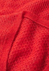 Gros plan sur un tissu rouge texturé, présentant un motif en maille lâche avec des fibres douces et duveteuses, affiché en plis superposés.