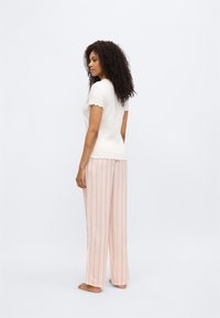 Άσπρο ριμπ κοντομάνικο τοπ με κυματιστά τελειώματα, συνδυασμένο με ροζ ριγέ παντελόνια με φαρδιά μπάτζια. Μαλακή υφή, άνετη εφαρμογή και διακριτική αντίθεση χρωμάτων.