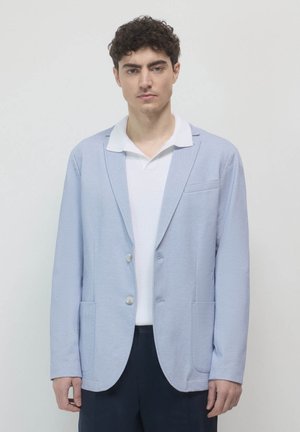 Light blue blazer made from textured fabric, featuring a two-button closure, notch lapels, and front patch pockets. Worn over a white polo.
