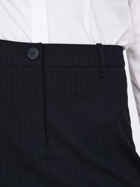 Hvid skjorte med knapper indstukket i sorte bukser med smalle striber, med en sort knap i midten og bærestrop på taljen.