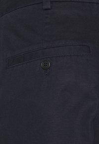 Tkanina námořnické modré barvy má hladký povrch, zadní kapsu s černým knoflíkem a jemné diagonální vzory.