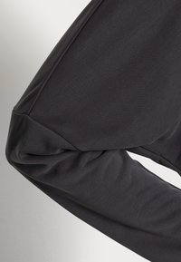 Svart bomullströja med lång ärm som har en åtsittande design, mjuk textur och rynkat accent vid ärmslutet.