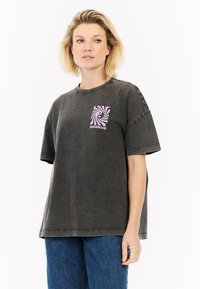 Donkergrijs oversized T-shirt van katoen, met een roze spiraalafbeelding op de linkerborst en korte mouwen.