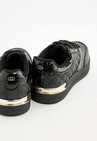 Mustad lakkjalatsid, millel on tekstureeritud krokodillimuster, vatitud külgedega ja kuldse tooni metalldetailid kontsas.