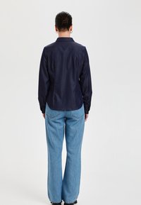 Camisa de manga larga azul marino con cuello, diseño ajustado y puños abotonados. Combinada con jeans de pierna ancha azul claro, mostrando la vista trasera.