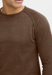 Brązowa koszula z długim rękawem wykonana z fakturowanej tkaniny, posiadająca okrągły dekolt oraz szwy w stylu raglanowym, o dopasowanym kroju.