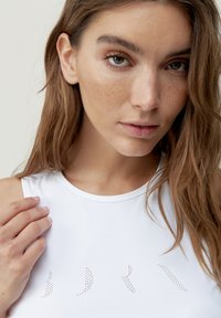 White sleeveless top with a rounded neckline, featuring small dotted patterns on the front and a smooth, soft texture.