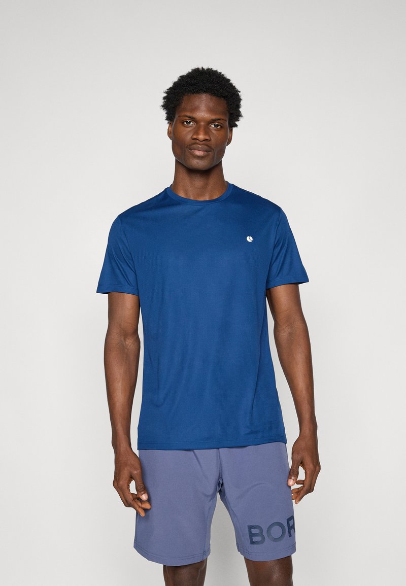 Navyblauw sportshirt met korte mouwen van ademend materiaal, met een klein logo op de borst, gecombineerd met lichtgrijze shorts met print.