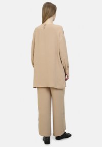 Abbigliamento beige e testurizzato composto da una lunga maglia con dettaglio a orecchio sul retro e pantaloni a gamba larga, abbinato a scarpe nere.