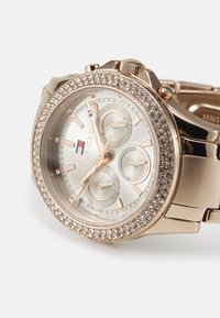 Montre plaquée or avec un cadran rond, une lunette scintillante et un cadran argenté. Comprend trois sous-cadrans et un bracelet en métal lié.
