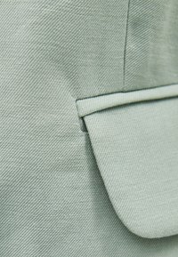 Zelená tkanina s texturovaným povrchem, s kapsou se rovnou klopou a čistými švy.