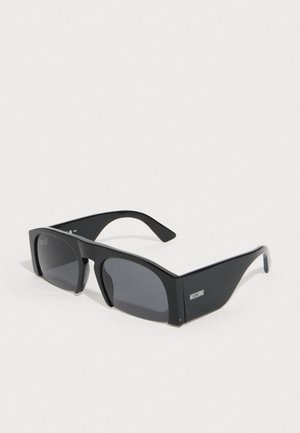 Crne sunčane naočale s geometrijskim dizajnom okvira, tamnim lećama i glatkom plastičnom površinom. Sadrže logo "Moschino" sa strane.