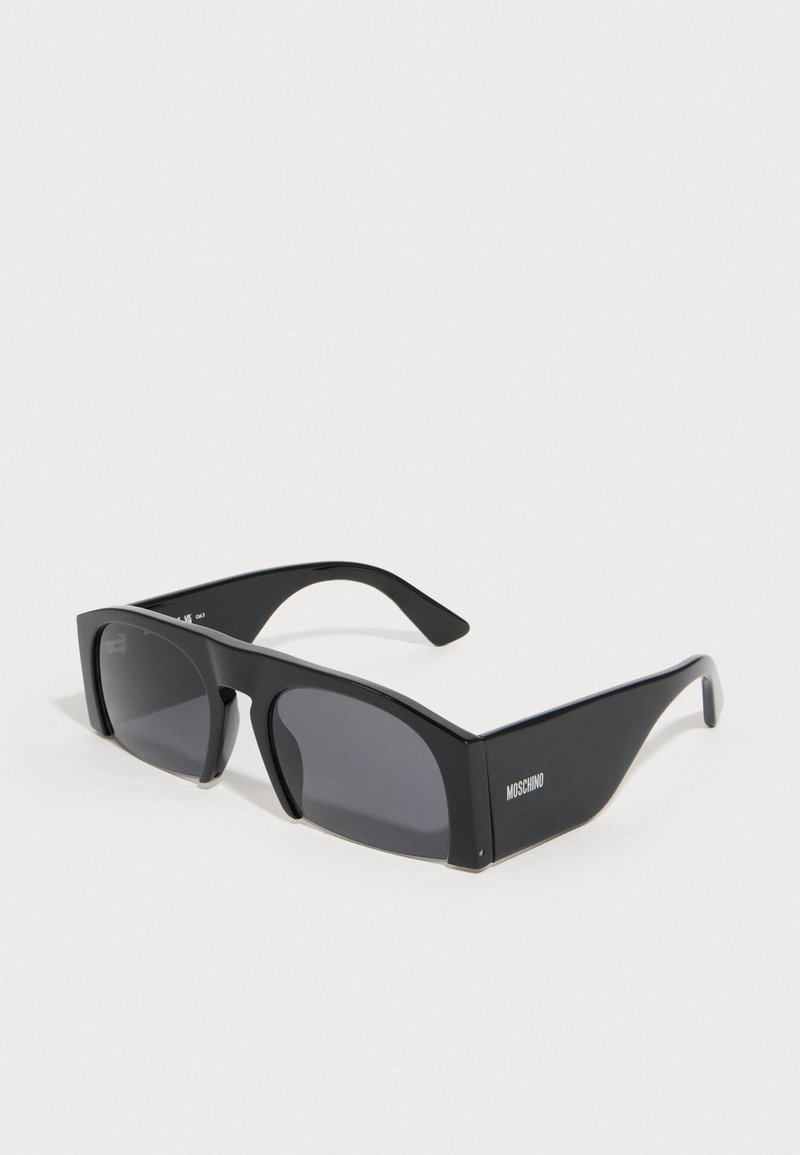 Melnas saulesbrilles ar ģeometrisku rāmja dizainu, tumšiem lēcām un gludu plastmasas apdari. Sānā redzams "Moschino" logotips.
