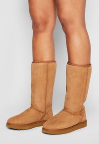 Stivali alti al ginocchio in suede beige con punta arrotondata e tomaia testurizzata. Presentano cuciture visibili e una suola in gomma per una migliore aderenza.