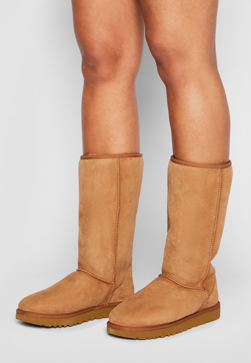 Stivali alti al ginocchio in suede beige con punta arrotondata e tomaia testurizzata. Presentano cuciture visibili e una suola in gomma per una migliore aderenza.